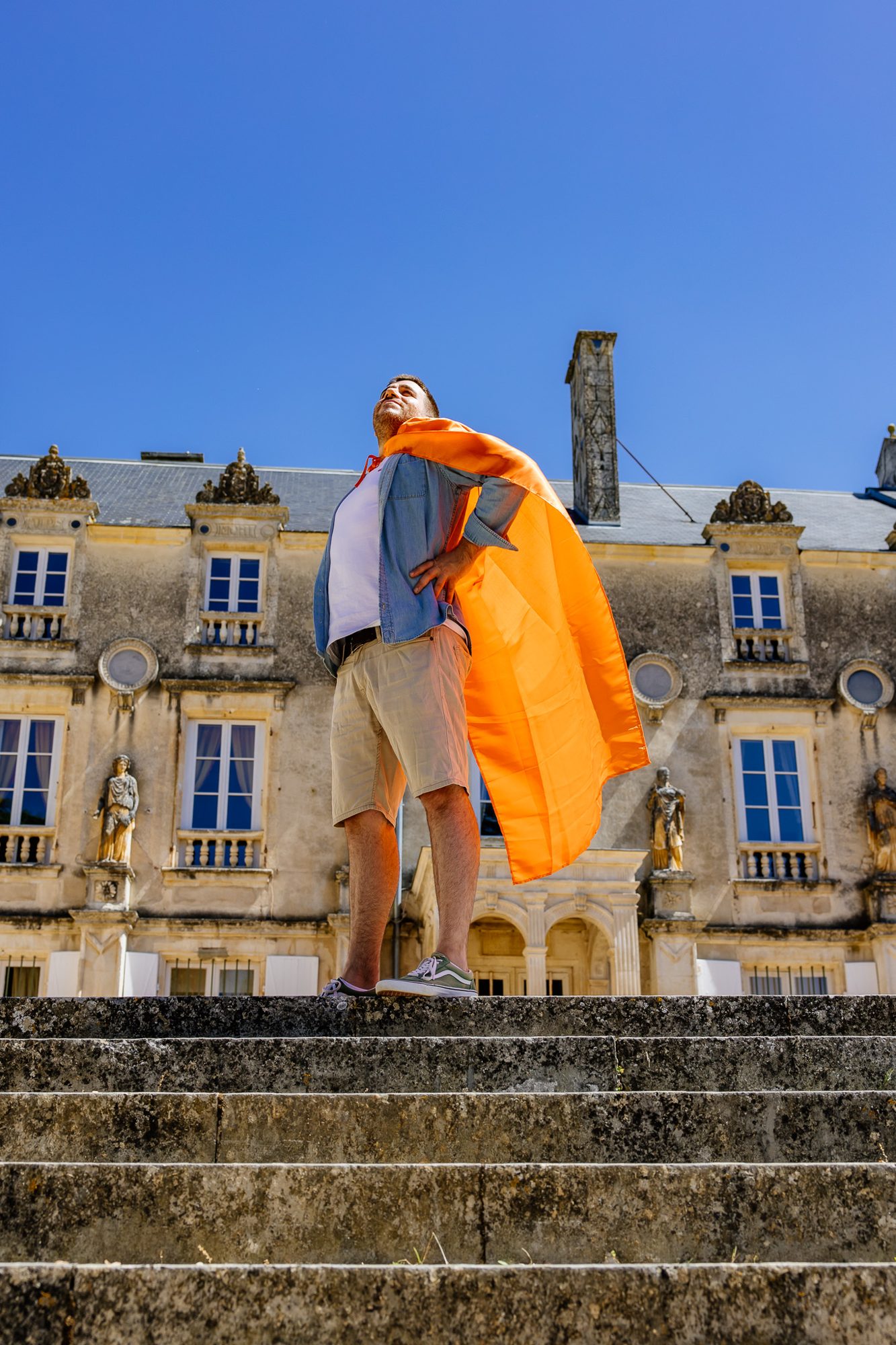 Homme en cape de super-héros orange devant un château